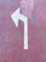 White left turn arrow on red textured asphalt road surface close-up