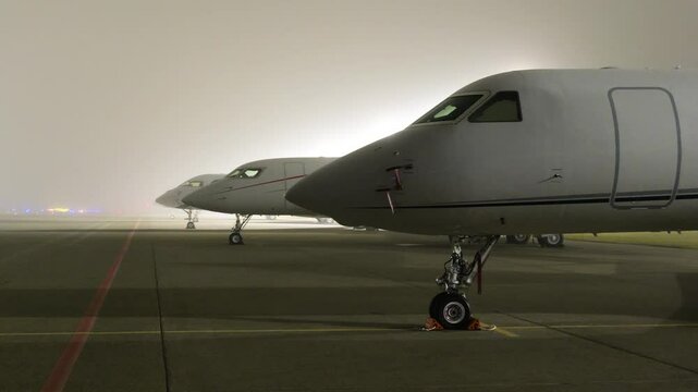 cockpit white heavy business jets aircraft parked apron fbo gat stands during dark night airport close up front panning shot area scene 