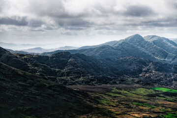 Obraz premium The Carrauntoohil Trail in Ireland, taking in breathtaking scenery of rugged hills and vibrant green fields under dynamic cloudy skies.