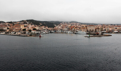 Naklejka premium A scenic view of La Maddalena town in Sardinia, Italy, captured from a ferry. The architecture, bay, and boats create a picturesque landscape, making it a perfect vacation destination.