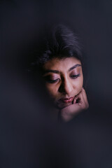 A woman with dark hair and brown eyes is looking down at her hands. The image has a mood of sadness and introspection