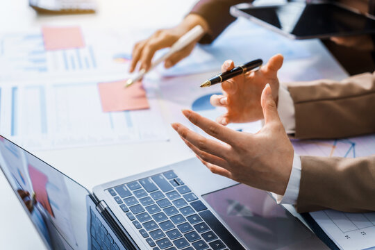 Two female business professionals in suits sit at desk, engaged in strategic discussion. They analyze financial planning, risk management, corporate growth while reviewing reports and market trends.