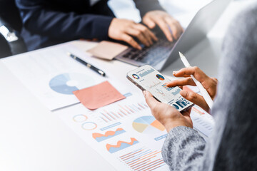 Two female business professionals in suits sit at desk, engaged in strategic discussion. They analyze financial planning, risk management, corporate growth while reviewing reports and market trends.