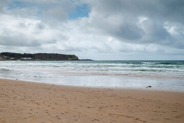 A panoramic view of White Park Bay, located on the Antrim Coast in Northern Ireland, featuring its sandy beach and rolling waves under a cloudy sky.