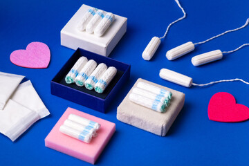 Fototapeta premium Hygienic tampons for protection during menstruation and everyday pads. Feminine hygiene concept. Tampons and pads on blue background, top view. Hygiene products for women. Women's health.