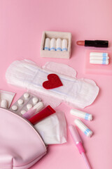 Сosmetic bag with cosmetics, painkillers pills, menstrual tampons, hygiene pads on pink background, top view. Hygiene and protection products for women during menstruation. Women's health.