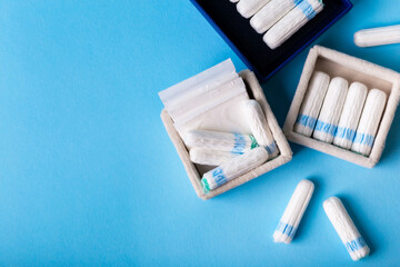 White sanitary tampons and everyday pads for women during menstruation on blue background, top view. Comfort, confidence and protection during menstruation. 