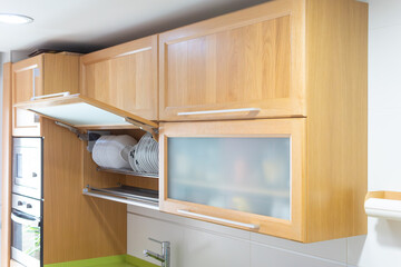 Italian design kitchen with oak wood hinged hanging cabinets with silver handles, green countertop and vertical column for oven and microwave.