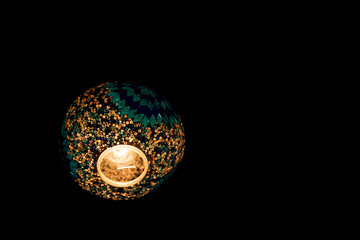 A lighted lamp with a blue and green design. The light is on and the lamp is sitting on a black background