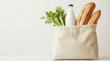 A minimalist display of a canvas bag filled with baguettes, a bottle of milk, and fresh celery against a neutral background