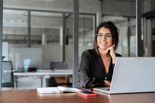 Portrait of smiling latin hispanic middle-aged business woman work on laptop computer in modern office. Indian young businesswoman professional employee using pc, looking dreaming aside. Copy space