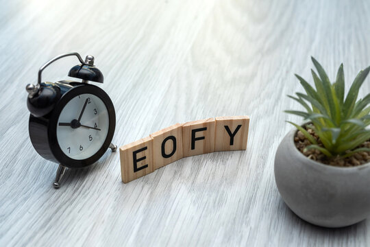 wooden word with text EOFY with Black mini alarm clock on desk. End of financial year on the note