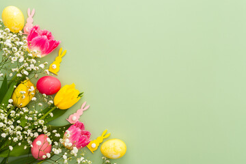 Spring Easter background, multi-colored Easter eggs with tulips and gypsophila and decorative bunnies on a green background