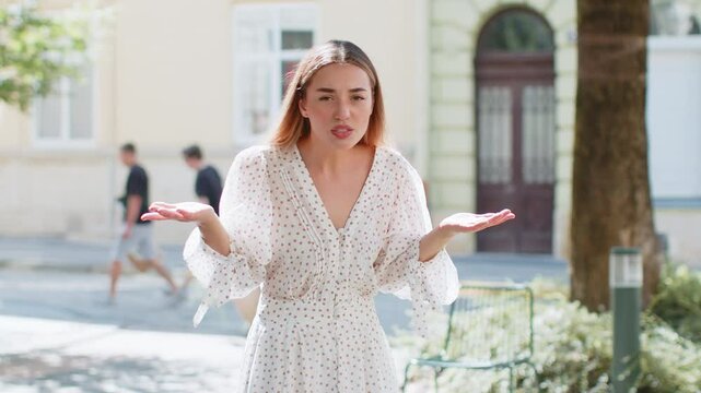 I don't know what to say. Confused young woman feeling embarrassed about ambiguous question having doubts no idea being clueless uncertain outdoors. Caucasian adult lady standing in urban city street.