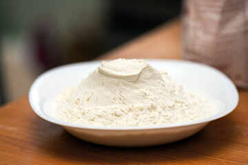 mound of wheat flour in a white ceramic bowl on a wooden table, showcasing its fine texture and natural color, perfect for baking and cooking