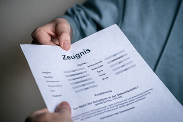 Nahaufnahme einer Zeugnisübergabe. Eine Person reicht einer anderen ein Schulzeugnis mit Notenübersicht. Das Bild steht für Bildung, Schulabschluss, Leistungsbewertung und akademische Erfolge.
