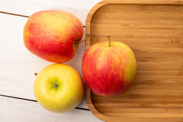 Three juicy apples with bamboo plate on wooden table, close-up, top view.