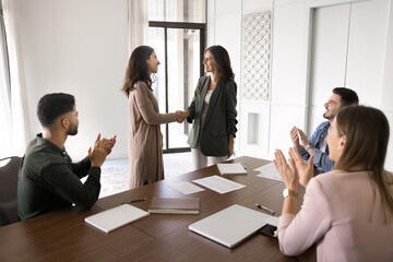 Company head welcoming staff member, standing in boardroom and shake hands to applauses of meeting...