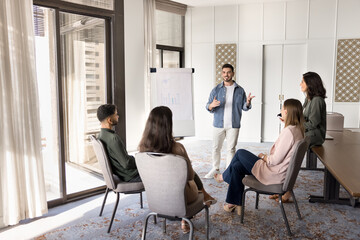 Young Arabian business coach making flip chart presentation standing in front of staff members,...