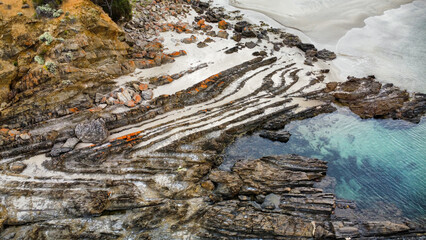 A rocky bay in Australia covered in orange lichen, seen from above