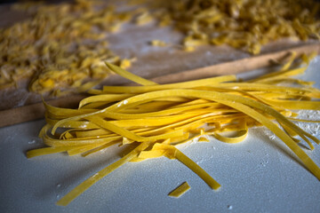 Bright yellow fresh handmade tagliatelle egg pasta drying on white rustic textured kitchen table
