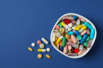 Various pills in a bowl on blue background, top view