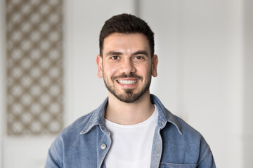 Young 25s Middle-Eastern man staring at camera while standing alone in office or domestic area,...