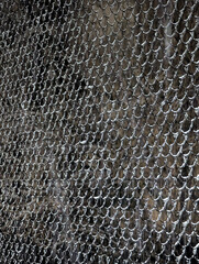 A close-up of a snow-covered metal mesh, a chain-link fence in winter, illuminated by the light of...