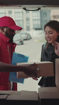 Portrait courier African American gives a parce to a woman after signing on delivery device cardboard technology box order post postal service device sunny beard covered load logistic mailman