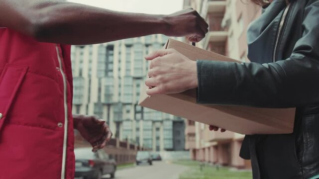Close up hands courier African American gives a parce to a woman after signing on delivery device cardboard technology box order post postal service device sunny beard covered load logistic mailman