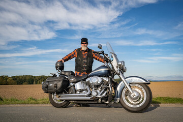 Fototapeta premium Cooler Motorradfahrer mit grauem Bart und Sonnenbrille präsentiert stolz sein klassisches Motorrad.