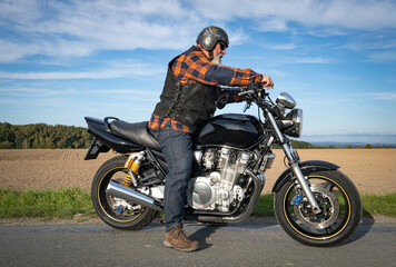 Obraz premium Cooler Motorradfahrer mit grauem Bart und Sonnenbrille präsentiert stolz sein klassisches Motorrad.