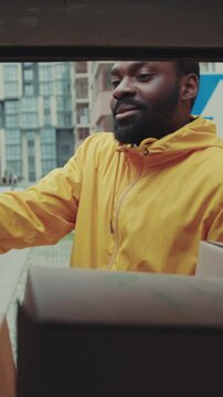 Smile courier African American open car gives a parce to a woman after signing on delivery device cardboard technology box order post postal service device sunny beard covered load logistic mailman