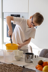 Young Boy Mixing Ingredients in Kitchen. A focused young boy wearing glasses and a white shirt...