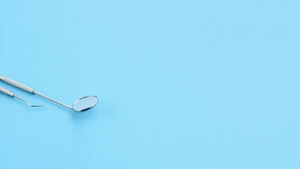 Fototapeta premium Dental hygiene tools, including a mirror and probe, isolated on a light blue background.