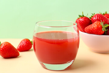 Glass of juice and bowl with strawberry on beige table