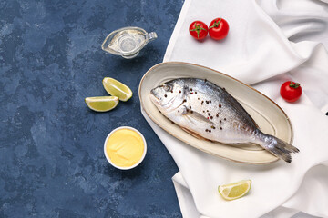 Plate of raw dorado fish with lime and sauce on blue background
