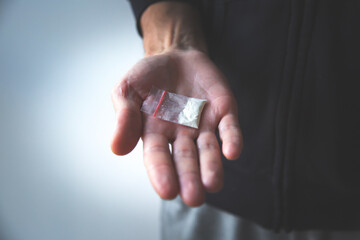 male hand holding a packet of white substance, drug in dark oppressive atmosphere