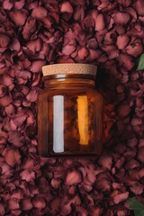 Amber glass jar lies on rose petals. Top view