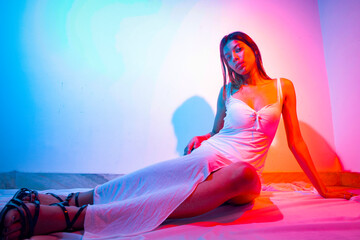 female model with long hair wearing a long white dress with a slit with a blue and red background