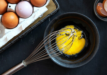 Beaten egg yolks in a bowl surrounded by fresh eggs on a dark kitchen countertop