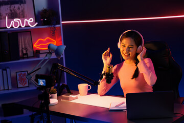 Smiling creative young beautiful Asian influencer talking in channel with positive podcast speech...