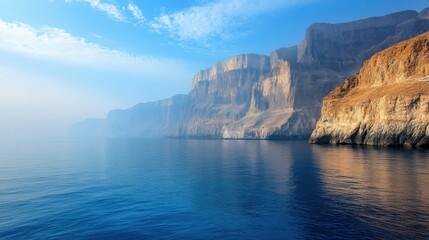 Obraz premium Ocean scene with cliffs. Calm water on rocks. Peaceful seascape at daytime. Blue sky above the landscape. Morning light on the mountain.