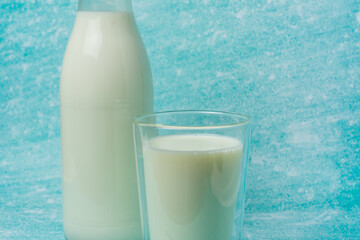 Full glass of milk sits next to a glass milk bottle on a blue surface. Scene evokes freshness and simplicity, perfect for dairy, breakfast, and healthy lifestyle themes.