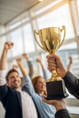 Close-up of hands holding a golden trophy cup. A team of employees celebrating their achievement and teamwork.