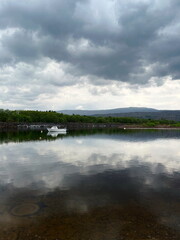 Fototapeta premium A lone white boat floating on the calm waters of the River Lochy near Inverlochy, Scotland, under a moody spring sky.