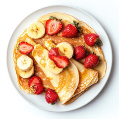 Overhead view of pancakes topped with sliced bananas and strawberries on a white plate