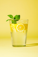 Glass of lemonade with mint against yellow background.