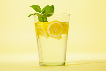 Glass of lemonade with mint against yellow background.