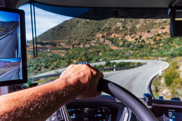 Driver's hand firmly gripping the steering wheel on a mountain descent with a sharp curve.